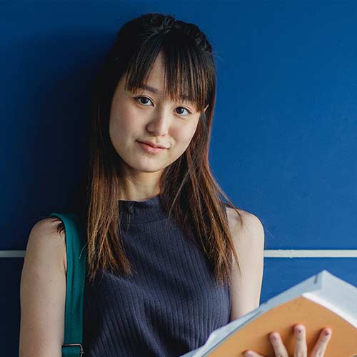 Jeune fille avec livre dans la main, elle nous regarde en souriant, studieuse